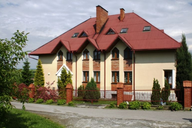 Zdjęcie budynku DPS Szczyrzyc - żółty budynek z czerwonym dachem a wokół roślinność