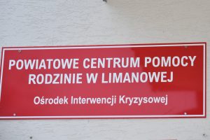 Tablica informacyjna na czerwonym tle napis Powiatowe Centrum Pomocy Rodzinie w Limanowej Ośrodek Interwencji Kryzysowej