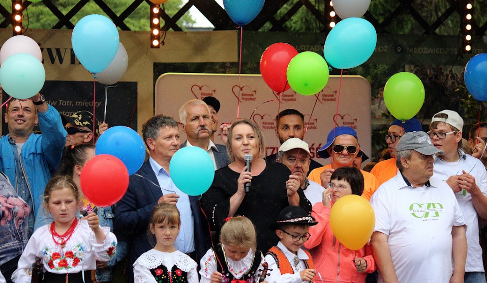 Grupa ludzi trzymających balony a jedna osoba przemawia przez mikrofon