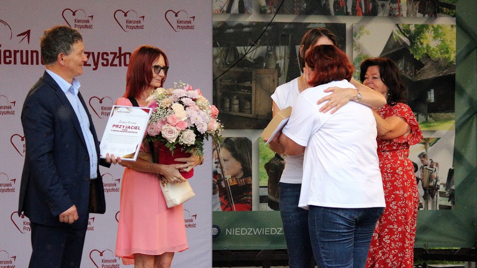 Grupa osób daje kwiaty i podziękowanie jednej kobiecie, która ze wzruszenia płacze