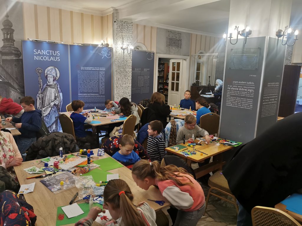 dzieci siedzą wokół stołów na warsztatach i wykonują prace ręczne