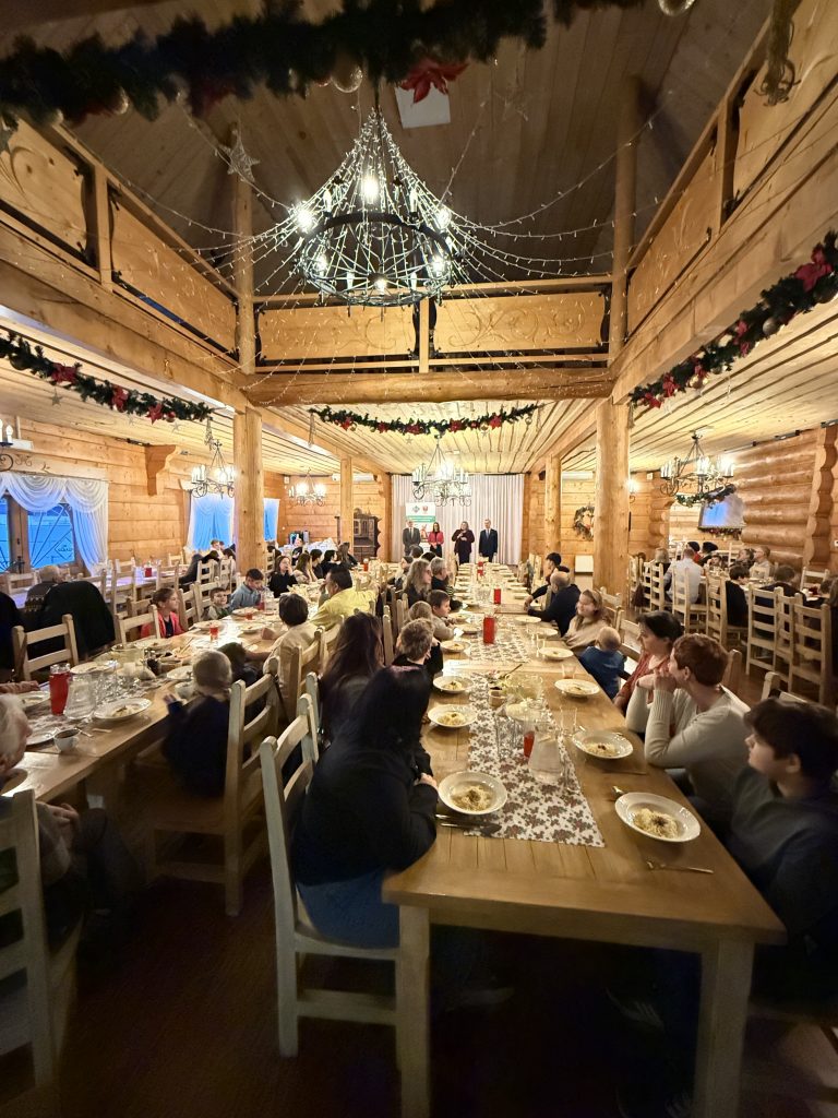 Rodzice i dzieci siedzą przy dużym długim stole i słuchają podziękowań i życzeń władz Powiatu