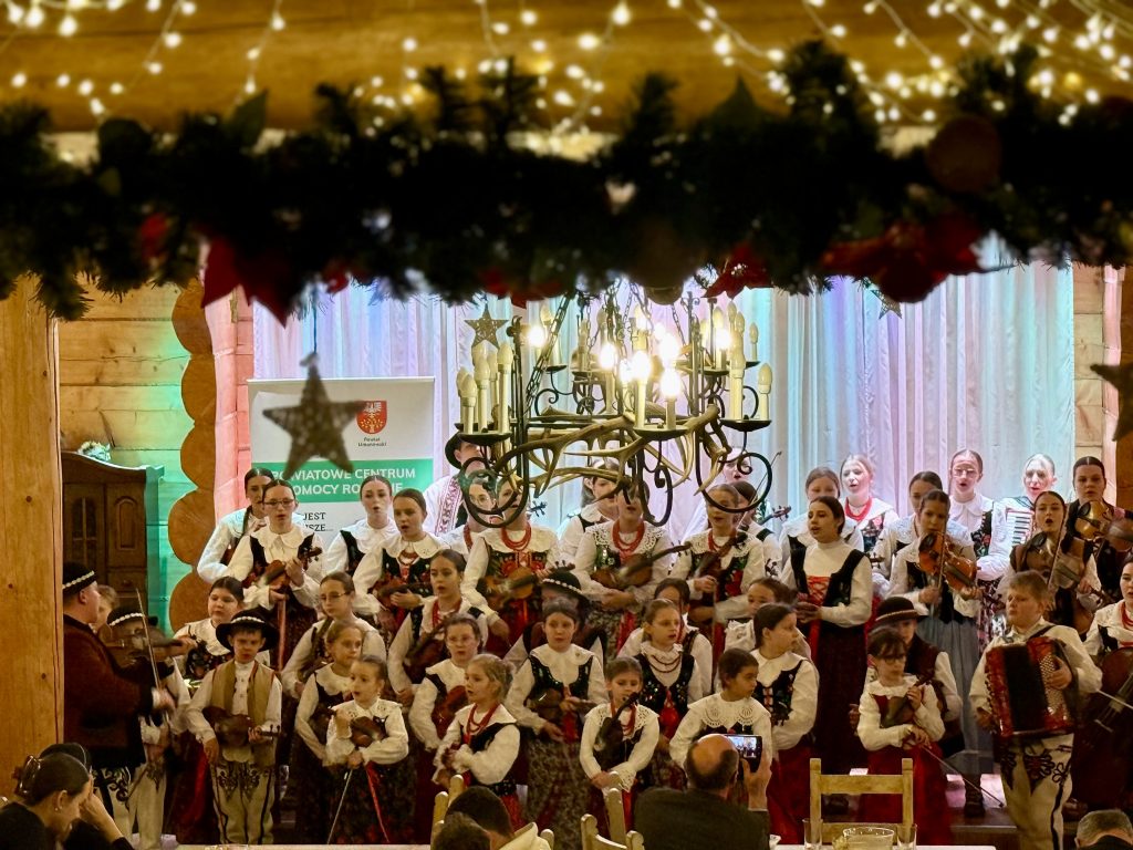 Grupa dzieci ubranych po góralsku grają na skrzypcach i spiewają